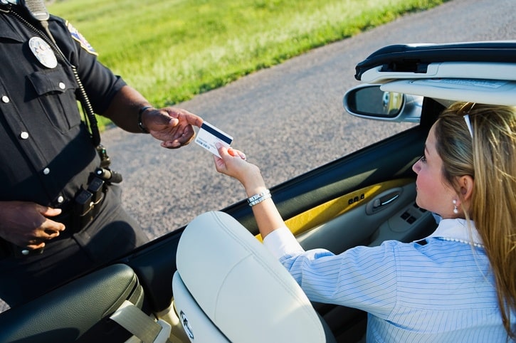 Mid adult woman sitting in a car giving her driver's license to a police officer