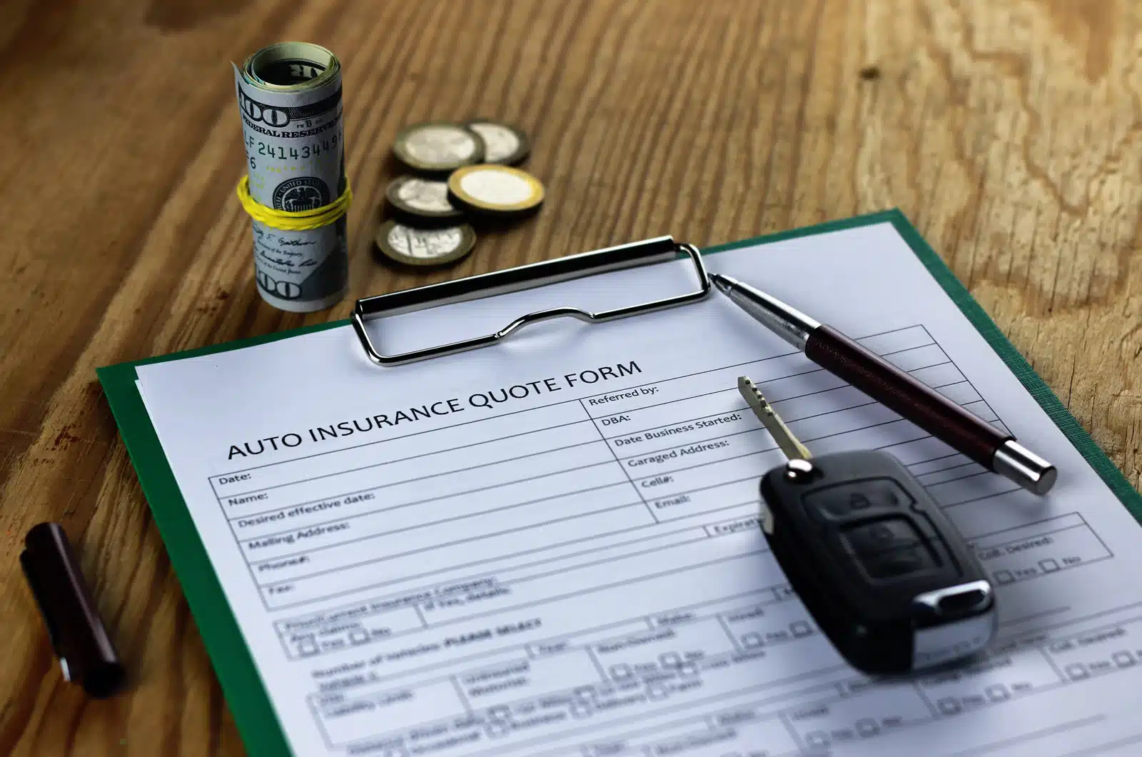 2026-09-sr-22-insurance-south-carolina-dui An auto insurance quote form on a green clipboard sits on a wooden table beside a car key, a pen, a rolled bundle of cash and loose coins.